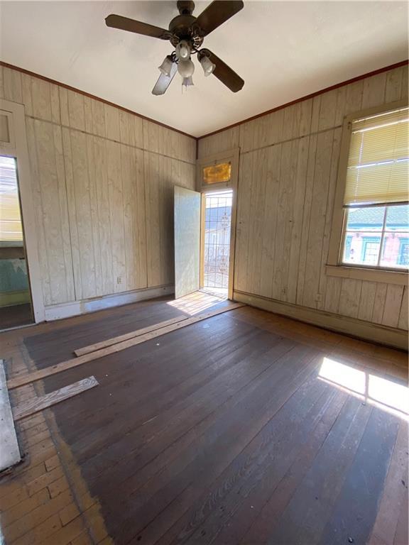 empty room with ceiling fan, dark wood-type flooring, and wood walls