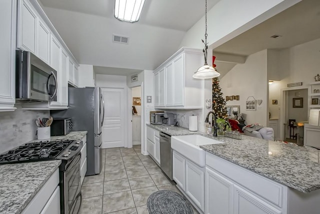 kitchen featuring pendant lighting, white cabinets, vaulted ceiling, light stone countertops, and appliances with stainless steel finishes