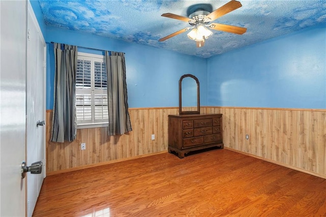 interior space with ceiling fan, wood-type flooring, a textured ceiling, and wooden walls