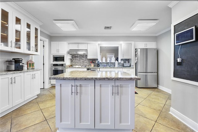 kitchen with under cabinet range hood, appliances with stainless steel finishes, white cabinets, and decorative backsplash