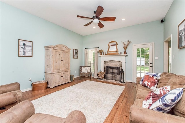 living room with ceiling fan, light hardwood / wood-style floors, and a brick fireplace