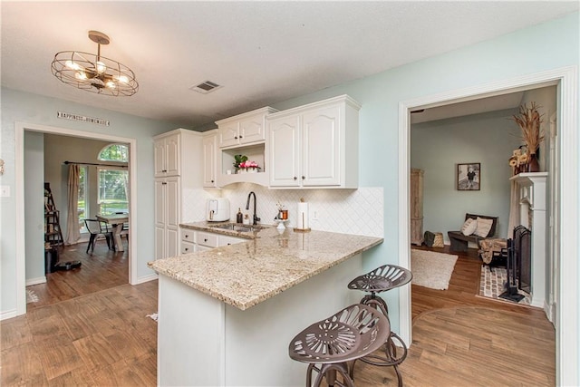 kitchen featuring decorative backsplash, light stone counters, sink, light hardwood / wood-style floors, and white cabinetry