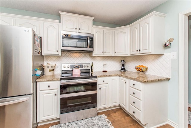 kitchen with decorative backsplash, light stone countertops, stainless steel appliances, hardwood / wood-style flooring, and white cabinets