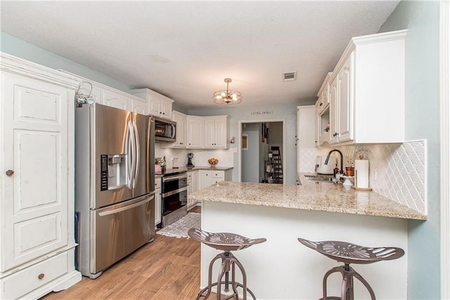 kitchen featuring kitchen peninsula, appliances with stainless steel finishes, white cabinetry, and sink