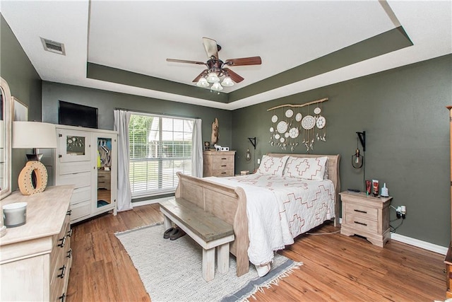 bedroom featuring ceiling fan, a raised ceiling, and wood-type flooring