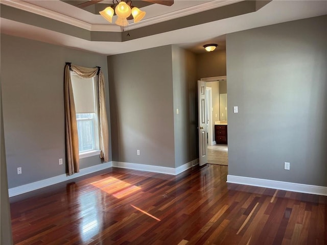 spare room featuring a tray ceiling, ceiling fan, dark wood-type flooring, and ornamental molding