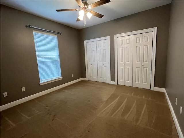 unfurnished bedroom with carpet flooring, ceiling fan, and multiple closets