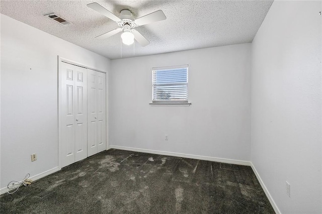 unfurnished bedroom featuring ceiling fan, dark carpet, a textured ceiling, and a closet