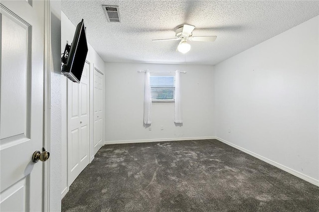 unfurnished bedroom featuring ceiling fan, dark carpet, and a textured ceiling