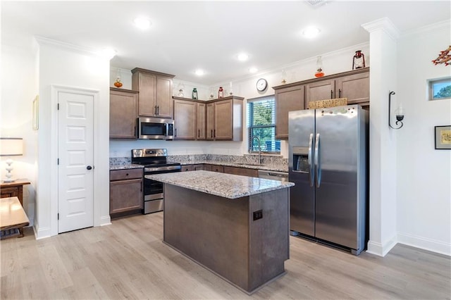 kitchen with ornamental molding, a kitchen island, stainless steel appliances, and light wood-type flooring