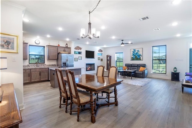 dining room with sink, ornamental molding, ceiling fan with notable chandelier, and light wood-type flooring