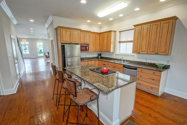 kitchen featuring a breakfast bar, sink, appliances with stainless steel finishes, a kitchen island, and dark stone counters