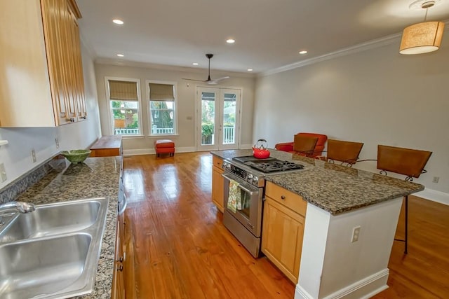 kitchen featuring sink, a kitchen breakfast bar, hanging light fixtures, light hardwood / wood-style floors, and gas range