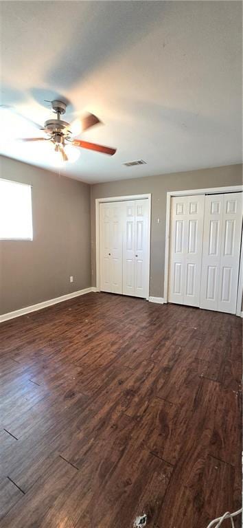 unfurnished bedroom featuring multiple closets, ceiling fan, and dark hardwood / wood-style flooring