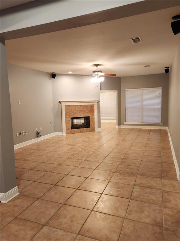 unfurnished living room with ceiling fan, light tile patterned floors, and a tile fireplace