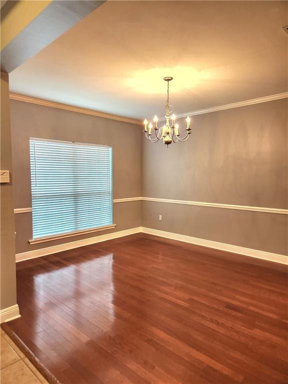 unfurnished room featuring ornamental molding, an inviting chandelier, wood finished floors, and baseboards