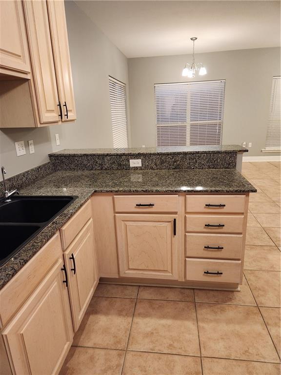 kitchen with sink, light brown cabinets, light tile patterned floors, decorative light fixtures, and dark stone countertops