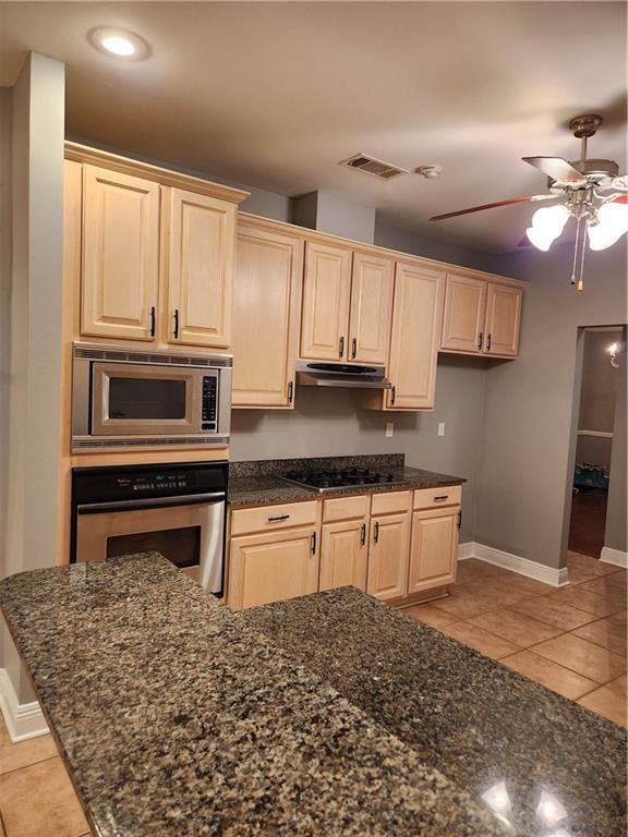 kitchen with ceiling fan, stainless steel appliances, dark stone counters, light brown cabinetry, and light tile patterned floors