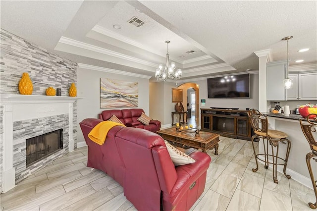 living room featuring an inviting chandelier, a stone fireplace, a raised ceiling, ornamental molding, and a textured ceiling