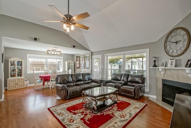 living room with hardwood / wood-style flooring, ceiling fan, a tiled fireplace, and vaulted ceiling