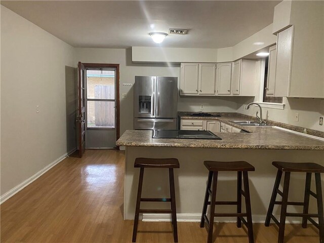 kitchen featuring stainless steel refrigerator with ice dispenser, a kitchen bar, dark wood-type flooring, sink, and kitchen peninsula