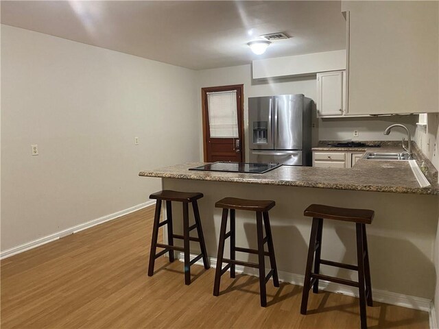 kitchen with black electric stovetop, sink, light hardwood / wood-style flooring, stainless steel fridge with ice dispenser, and a breakfast bar area