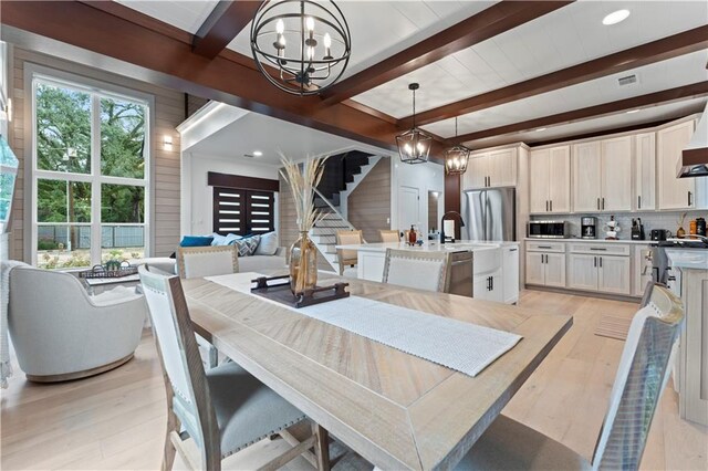 dining area featuring light hardwood / wood-style floors, beam ceiling, wooden walls, and an inviting chandelier