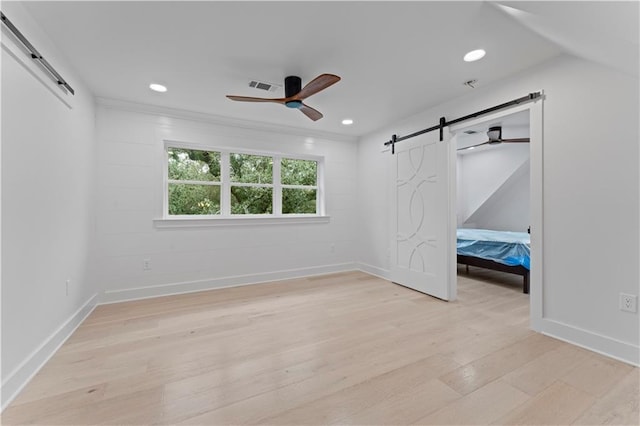 unfurnished bedroom featuring a barn door, light hardwood / wood-style flooring, and ceiling fan