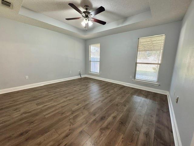 empty room featuring a textured ceiling, dark hardwood / wood-style floors, a raised ceiling, and ceiling fan