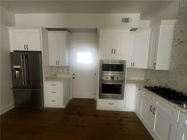 kitchen with appliances with stainless steel finishes, dark hardwood / wood-style flooring, tasteful backsplash, light stone counters, and white cabinetry