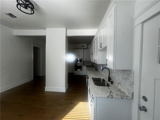 kitchen with sink, decorative backsplash, dark hardwood / wood-style floors, light stone counters, and white cabinetry