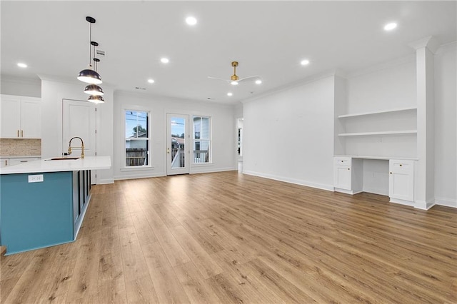 unfurnished living room with built in shelves, ceiling fan, sink, light hardwood / wood-style flooring, and ornamental molding