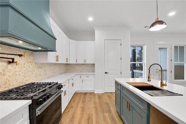 kitchen with premium range hood, high end stainless steel range oven, sink, pendant lighting, and white cabinetry