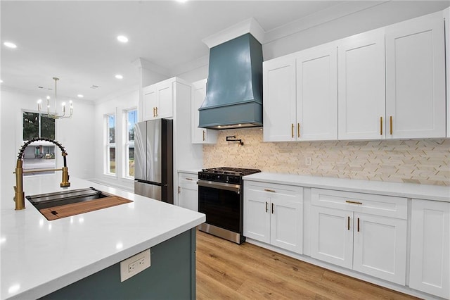 kitchen featuring white cabinetry, sink, appliances with stainless steel finishes, custom range hood, and light wood-type flooring