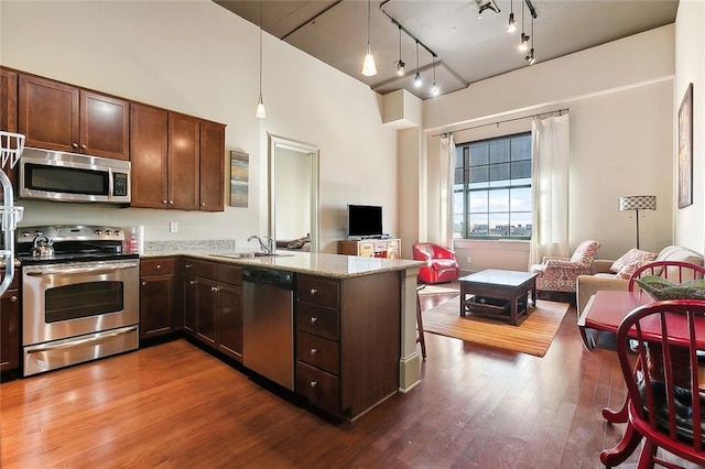 kitchen featuring light stone countertops, stainless steel appliances, sink, wood-type flooring, and decorative light fixtures