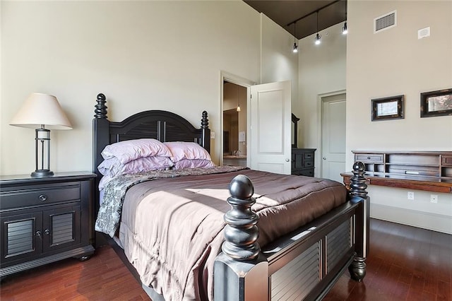 bedroom featuring dark hardwood / wood-style flooring, a towering ceiling, and ensuite bath