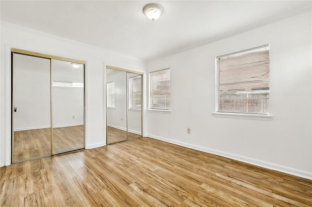 unfurnished bedroom with two closets and light hardwood / wood-style flooring