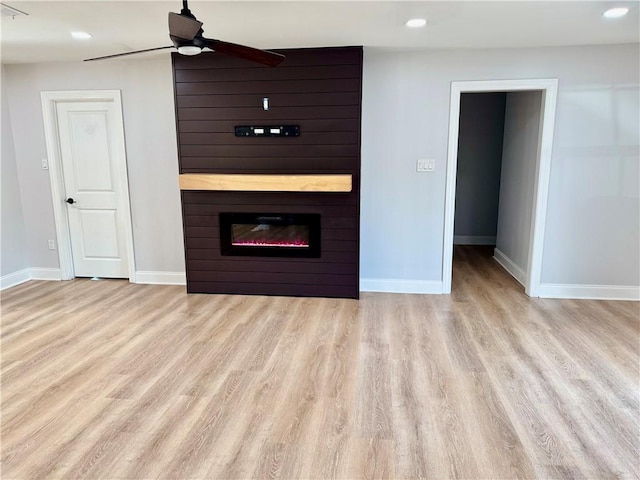 unfurnished living room featuring light hardwood / wood-style flooring, a large fireplace, and ceiling fan