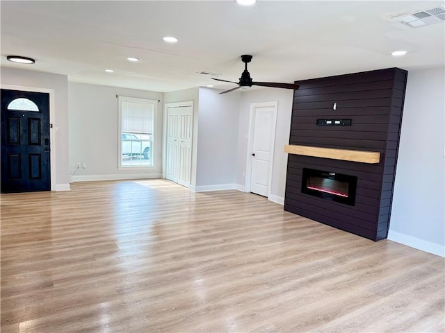 unfurnished living room with ceiling fan, a large fireplace, and light hardwood / wood-style flooring