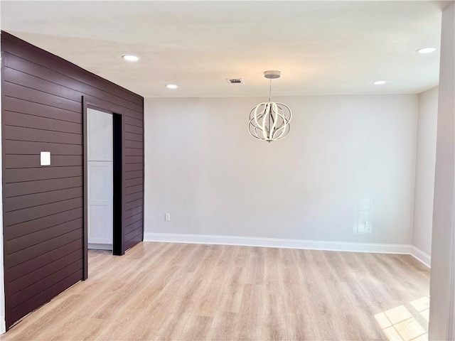 empty room featuring a notable chandelier, light hardwood / wood-style floors, and wood walls