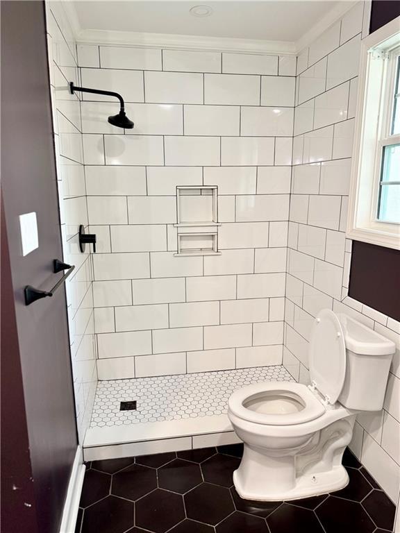 bathroom featuring tile patterned flooring, ornamental molding, toilet, and tiled shower