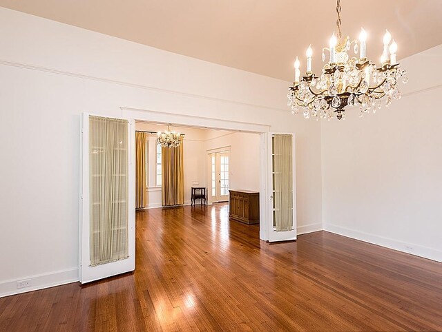 empty room featuring dark wood-type flooring, an inviting chandelier, and french doors