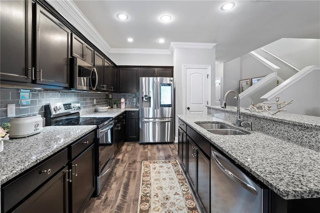 kitchen with ornamental molding, stainless steel appliances, a kitchen island with sink, dark wood-type flooring, and sink