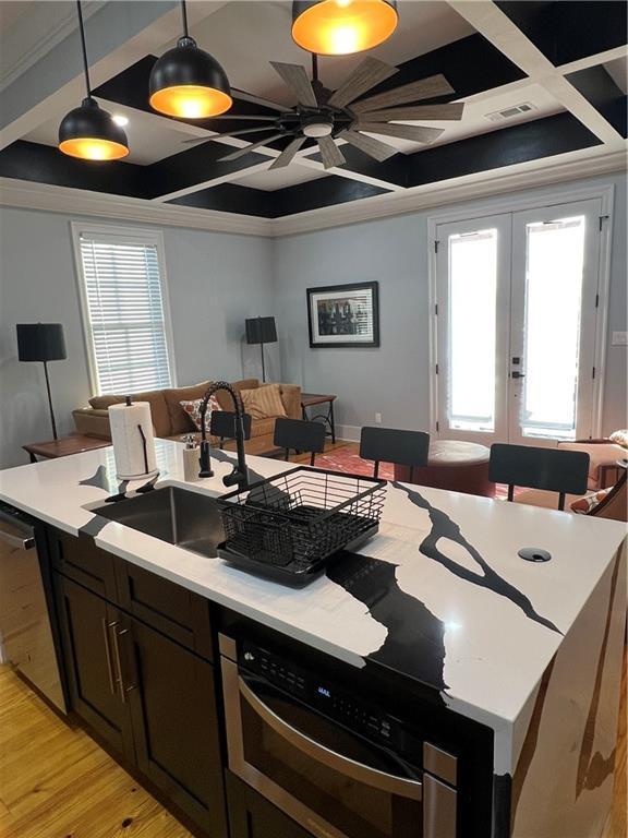 kitchen with coffered ceiling, sink, stainless steel dishwasher, light wood-type flooring, and decorative light fixtures