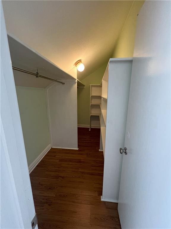 walk in closet with dark wood-type flooring and vaulted ceiling