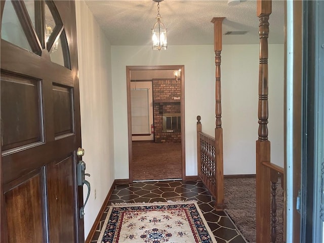 foyer featuring dark colored carpet, an inviting chandelier, a textured ceiling, and a brick fireplace