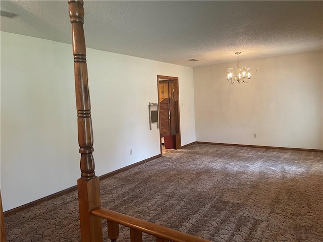 empty room with dark carpet, a textured ceiling, and an inviting chandelier