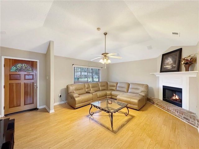 living room featuring ceiling fan, wood-type flooring, vaulted ceiling, and a brick fireplace