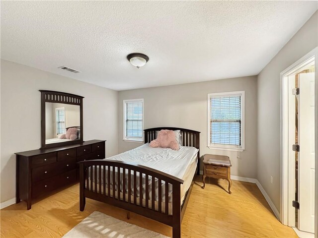 bedroom with light hardwood / wood-style floors, a textured ceiling, and multiple windows