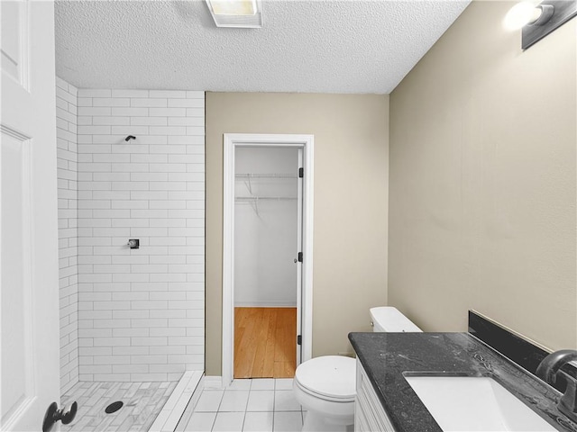 bathroom featuring vanity, tile patterned floors, toilet, a textured ceiling, and a tile shower